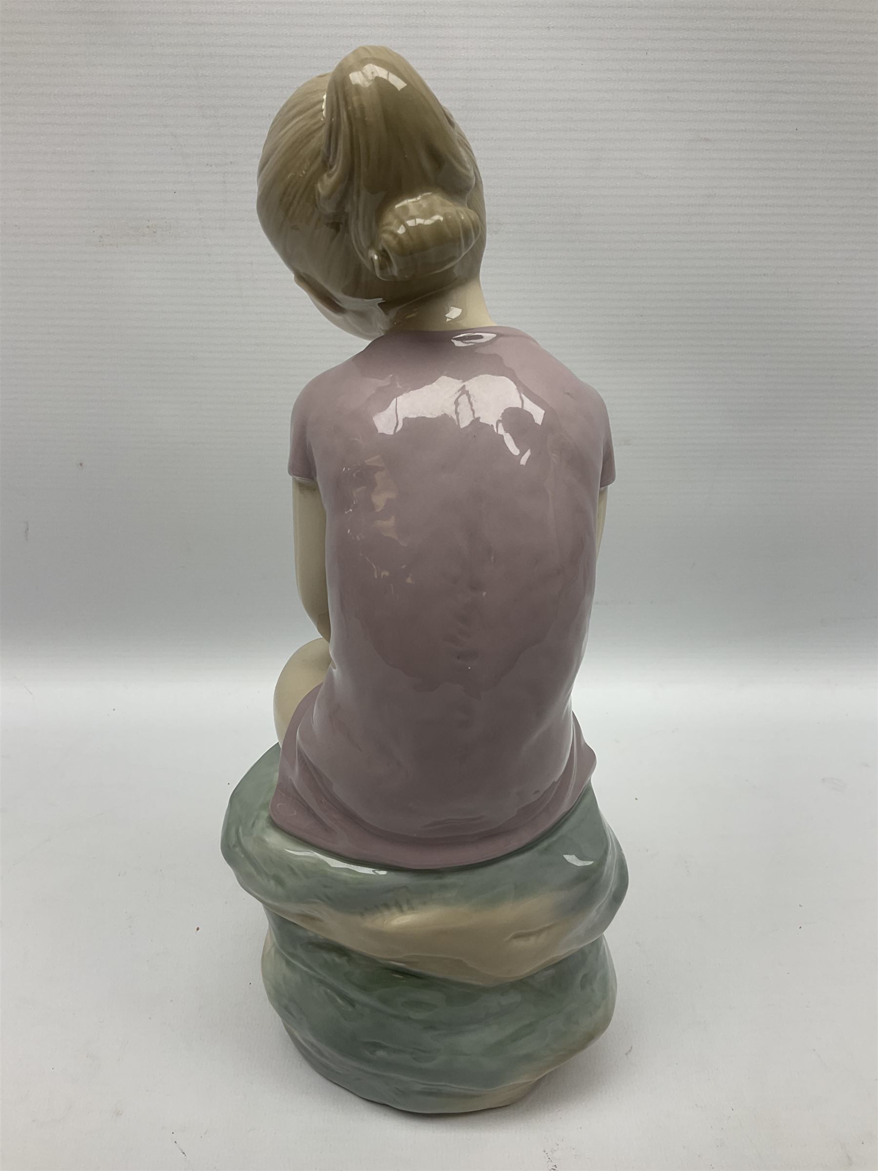 Large Nao figure modelled as a young girl seated upon a rock holding a rose, H30cm