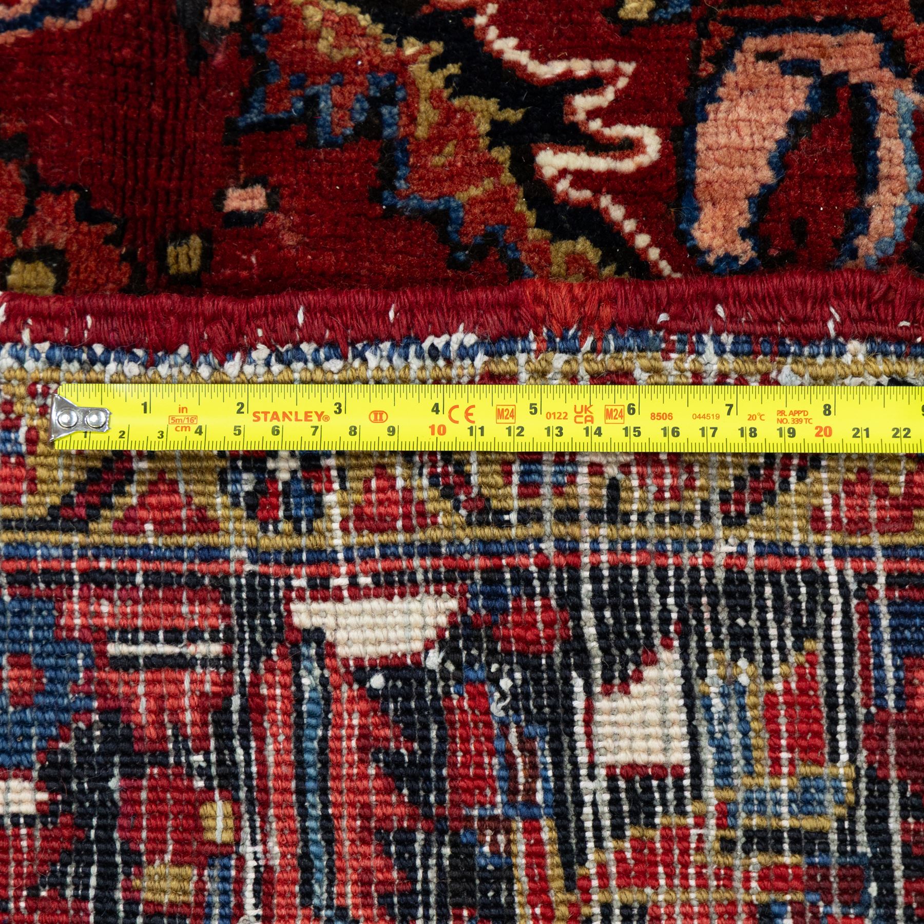 North West Persian Ahar hand-knotted carpet, madder red ground, with a large central shaped floral medallion with pendants, surrounded by angular scrolling foliate motifs incorporating rosettes, palmettes and stylised flowerheads, enclosed by ivory spandrels and a dark navy border with repeating geometric floral motifs and meandering vines, flanked by narrow patterned guard stripes, with cotton fringes