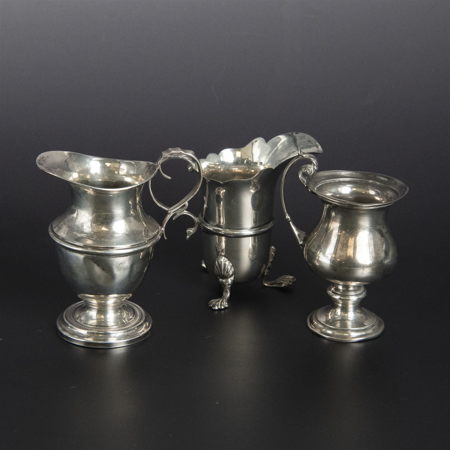 Group of early 20th century silver, comprising sauce boat, with flying scroll handle and upon three pad feet, two small cream jugs and a christening mug, all hallmarked, tallest H10cm