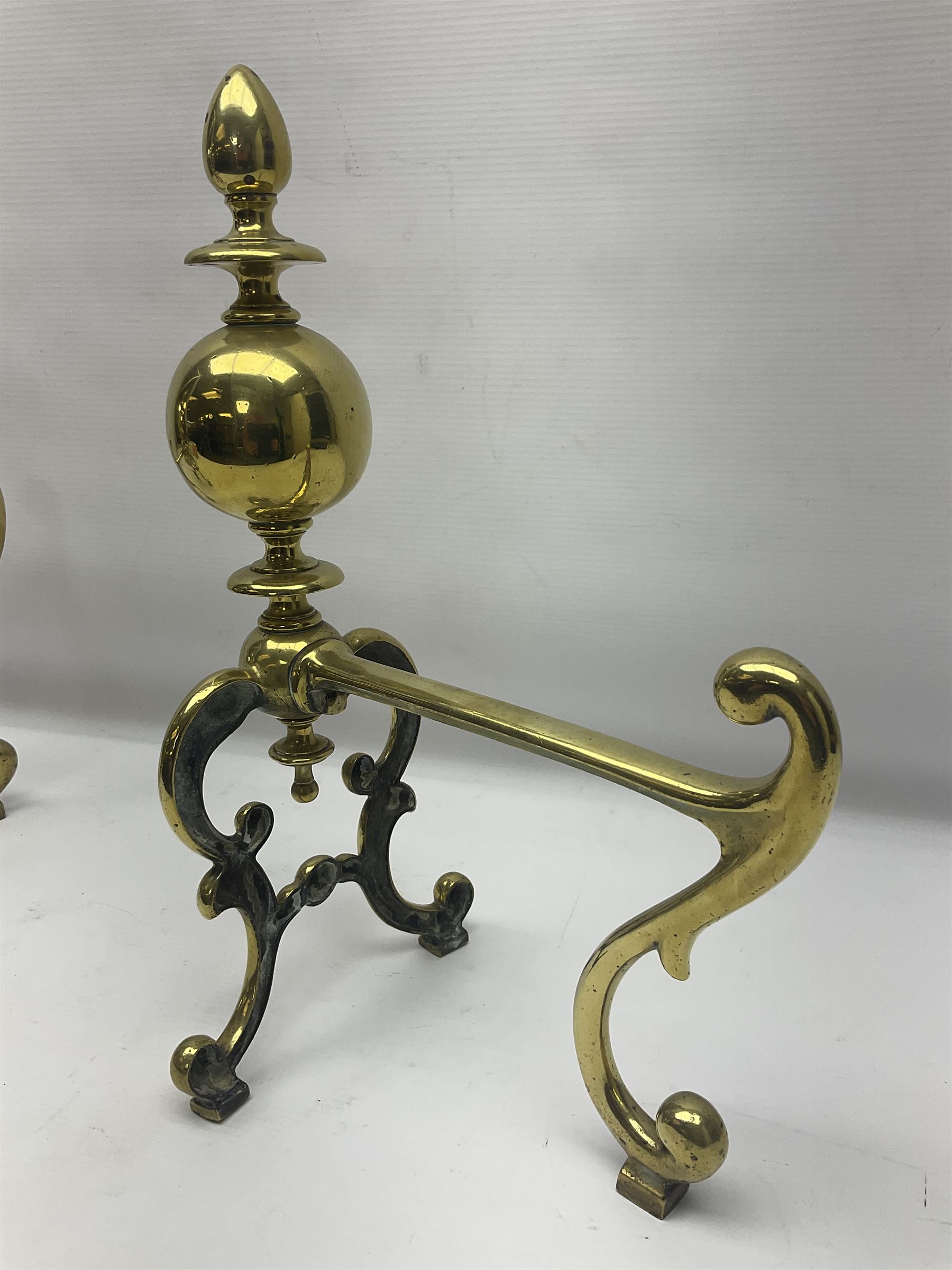 Pair of early 20th century brass fire dogs, each with sphere and urn finial, upon a scrolling base, H38cm