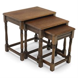 Nest of three dark oak tables, rectangular top with turned supports, tables suspended on rails
