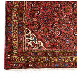 Hamadan hand-knotted rug, red field with small central floral medallion and dense repeating geometric motifs in dark blue, cream and green tones, within multiple patterned borders