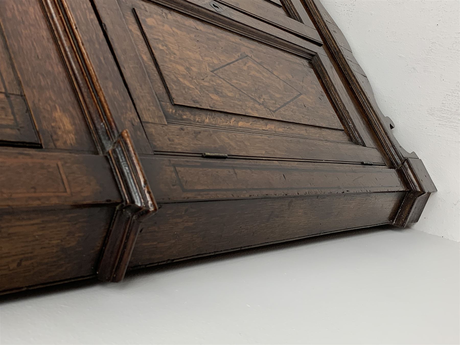 George III oak floor standing corner cabinet, scrolled swan neck pediment with central finial over astragal glazed door, painted interior fitted with three shaped shelves, the lower section fitted with single shaped shelf enclosed by two fielded panel doors inlaid lozenges, on bracket feet, H195cm, W77cm