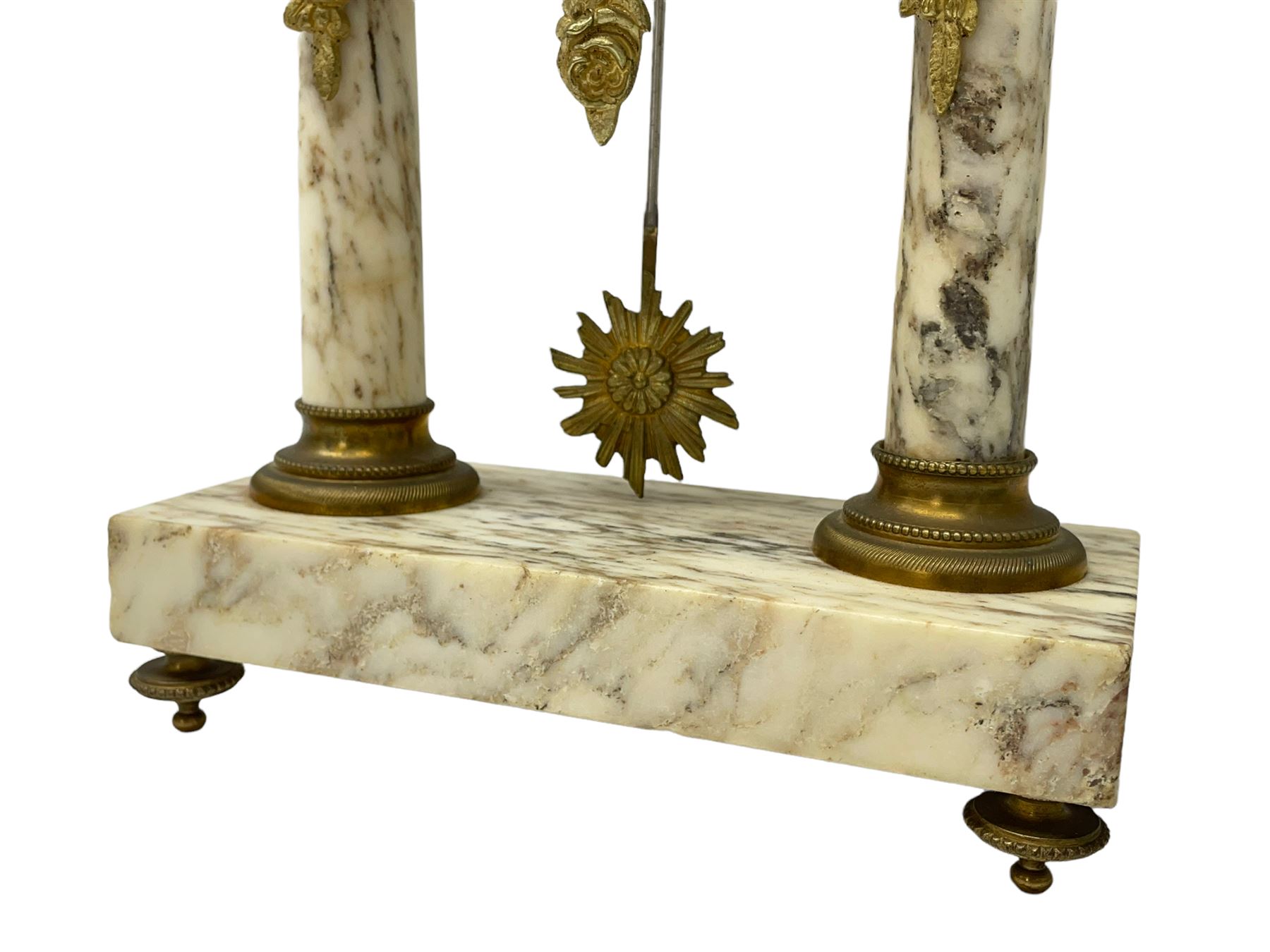 20th century French portico clock c1910 on a white veined marble base, gilt drum movement case supported between two marble columns with brass capitals and a suspended garland swag with a starburst pendulum beneath, enamel dial with Arabic numerals, floral decoration and Louis XV pierced gilt hands, convex glass and brass bezel, 8-day countwheel striking movement striking the hours and half hours on a bell. 




