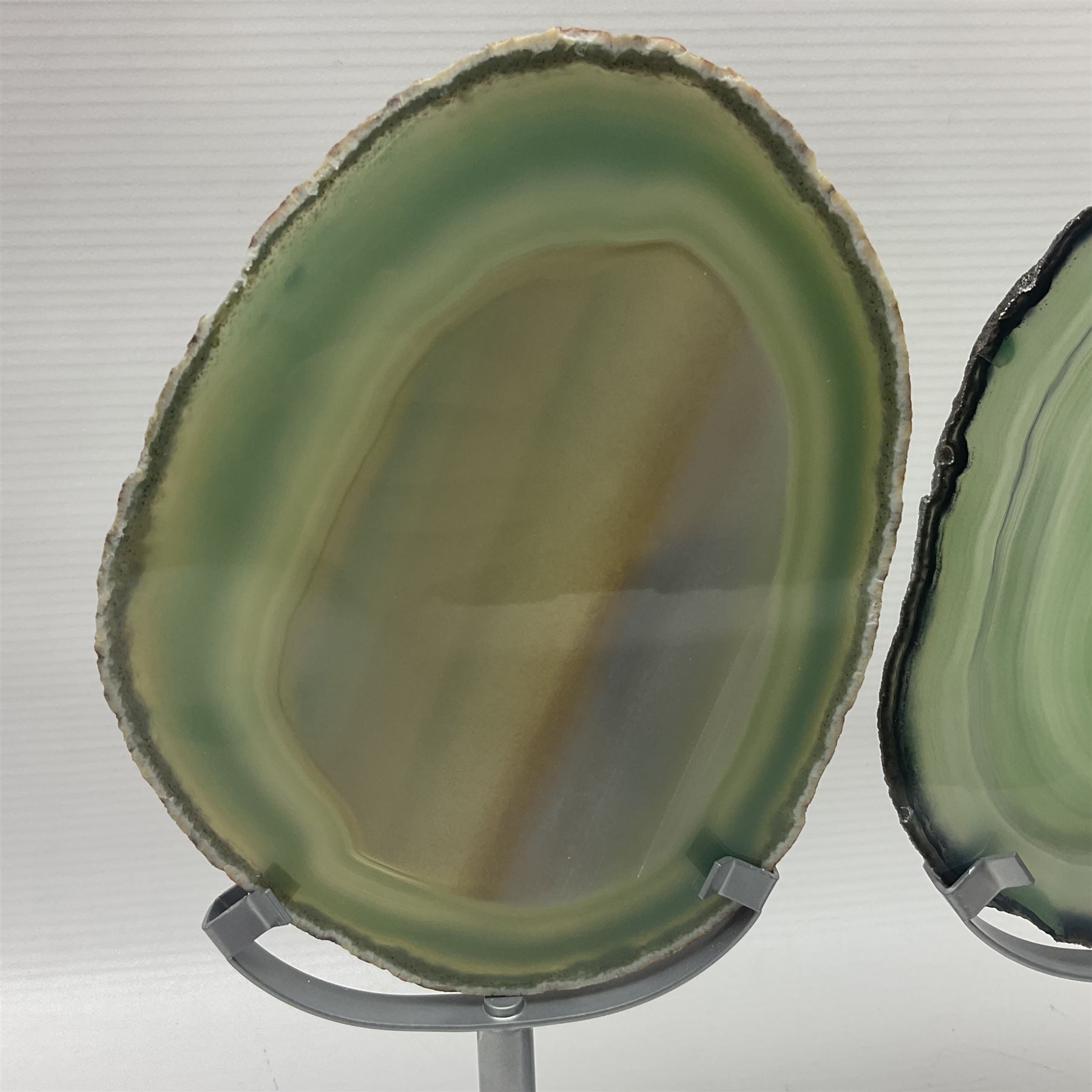 Pair of green agate slices, polished with rough edges raised upon silvered metal stands, H19cm