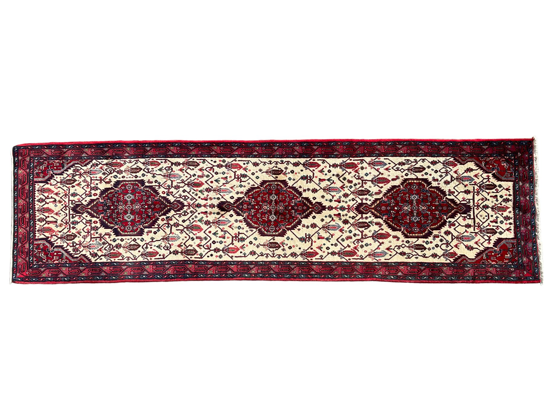 North West Persian Saveh crimson ground runner rug, the three lozenge pole medallions in an ivory field, surrounded by stylised plant motifs, the guarded border decorated with repeating geometric patterns