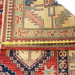 Caucasian Kazak hand-knotted rug, madder red field with bold geometric medallions and angular tribal motifs, within multiple patterned borders in a palette of indigo, red, ivory and green 