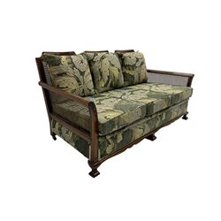 Early 20th century bergère lounge suite, mahogany framed with cane work back and sides, acanthus scroll carved uprights - three seat sofa (W167cm, H82cm, D83cm), and pair matching armchairs (W78cm), loose cushions upholstered in acanthus leaf scroll fabric with scatter cushions