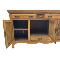 Edwardian light oak sideboard, two outer cupboards carved with scrolling motifs, enclosing smaller central cupboard above single drawer, all beneath two further drawers