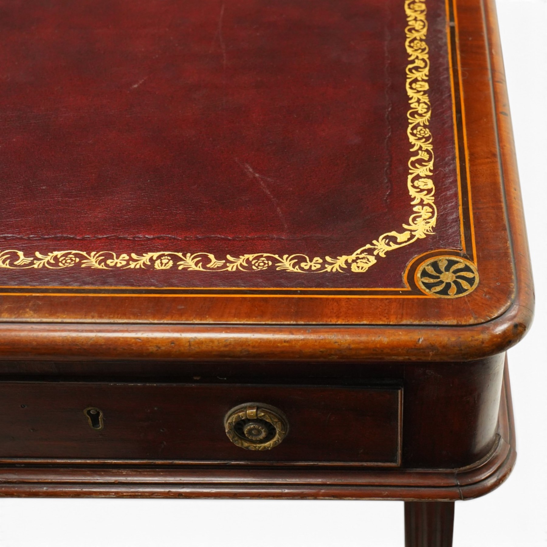 Regency inlaid mahogany and brass mounted library table, the rectangular top inset with gilt tooled burgundy leather writing surface, enclosed by  crossbanding and boxwood stringing with roundel corner motifs, above three cock-beaded frieze drawers to either side fitted with brass ring handles and brass escutcheons, the end friezes centred by applied brass foliate mounts, raised on twin reeded column supports over rectangular platform ends, united by a ring-turned stretcher, the reeded sabre legs terminating in brass caps and castors, one drawer bearing ivorine label 'Spillman & Co., St Martins Lane, London'