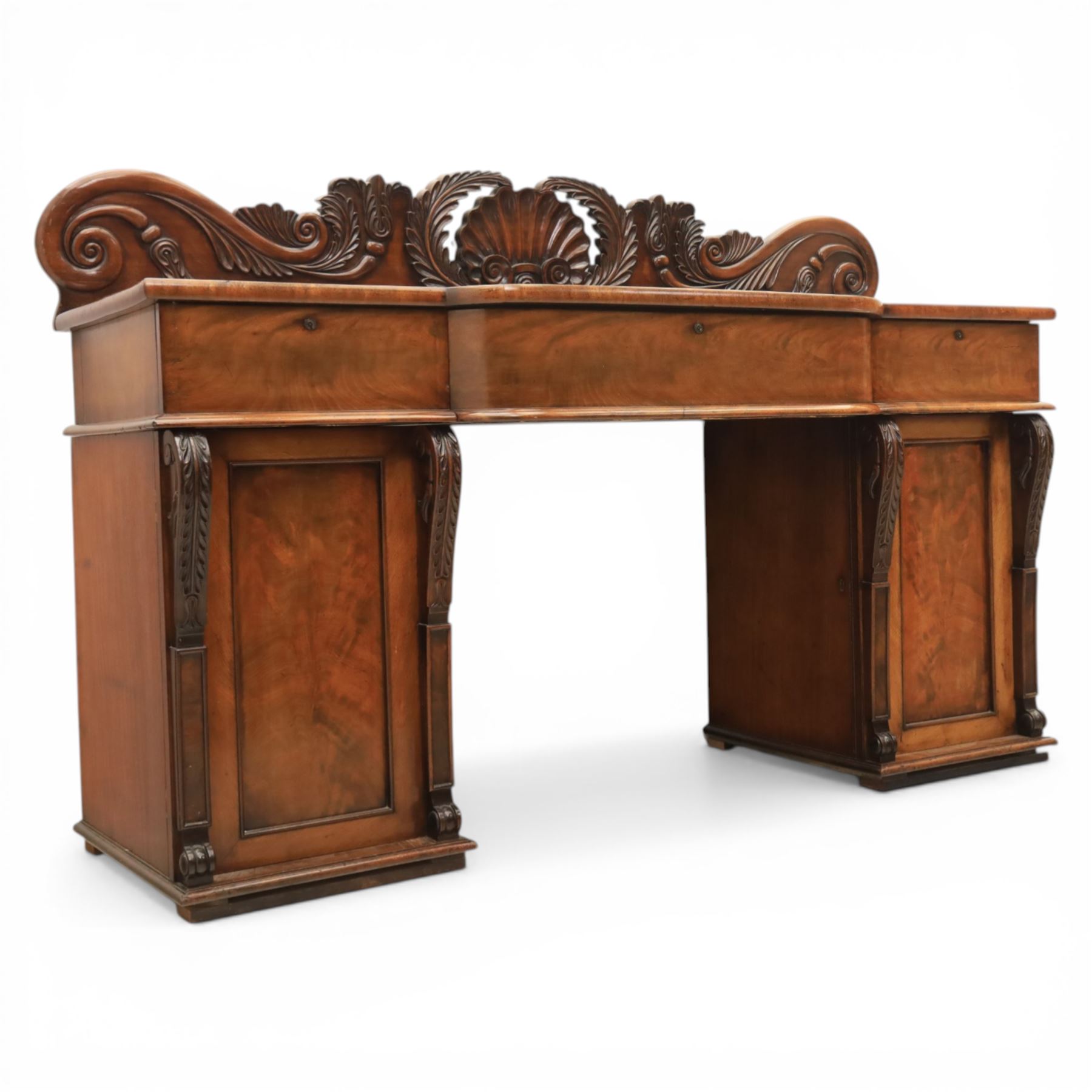 Mid Victorian mahogany pedestal sideboard, the rectangular top with raised back centred by a carved shell within scrolling acanthus and foliate cresting, over a central shaped frieze drawer flanked by two short drawers, above a kneehole recess, flanked by panelled cupboard doors with carved corbel supports, enclosing shelved interiors