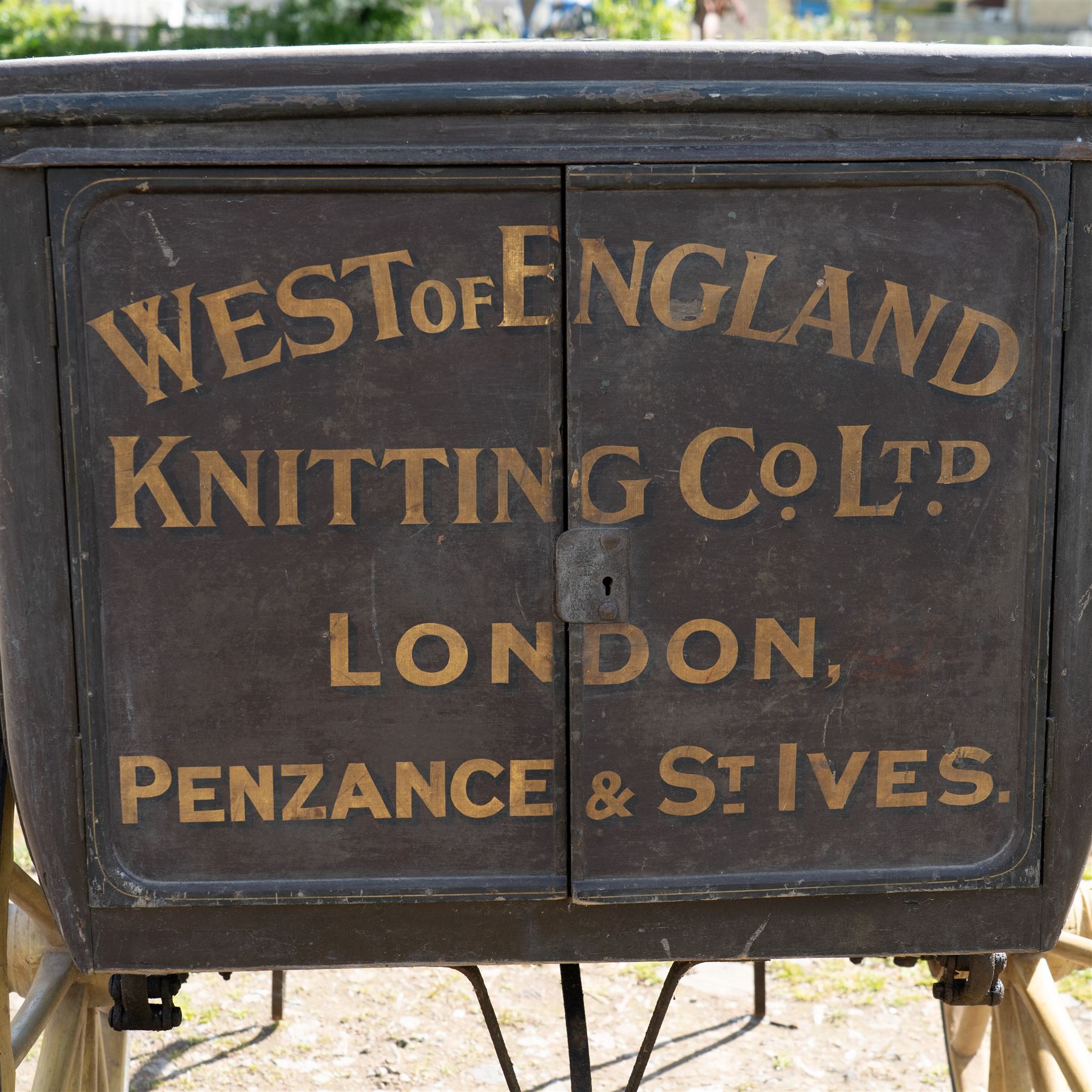 West of England Knitting Co. Ltd. Advertising Hand Cart

A rare and highly decorative late Victorian or Edwardian advertising hand cart, retaining its original black painted finish and gilt signwriting for West of England Knitting Co. Ltd., London, Penzance & St Ives. The enclosed box body is mounted on large cream painted wooden spoked wheels and fitted with rear push handles, allowing the cart to be manoeuvred by hand. Intended as a promotional and delivery vehicle for one of Britain's best known knitwear manufacturers, the cart survives as an evocative piece of commercial advertising history. The interior remains accessible via twin rear doors, while traces of the original maker's transfer for the Warwick Carrier are visible. An unusual and attractive display piece suited to collectors of advertising, transport memorabilia and social history.

Features

• Original hand painted gilt signwriting for West of England Knitting Co. Ltd.
• Advertising panels referencing London, Penzance and St Ives
• Enclosed wooden box body with twin rear access doors
• Original black painted finish with period lettering
• Large cream painted wooden spoked wheels with iron tyres
• Rear push handles for hand propelled operation
• Warwick Carrier maker's transfer remains visible
• Original undercarriage and running gear
• Attractive display piece with strong commercial advertising appeal
• Suitable for museum, retail, interior or collection display

Dimensions:
Overall length: 190 cm
Body length: 125 cm
Overall width: 140 cm
Body width: 100 cm
Height: 150 cm

Wheel Diameter:
Wheels: 92 cm