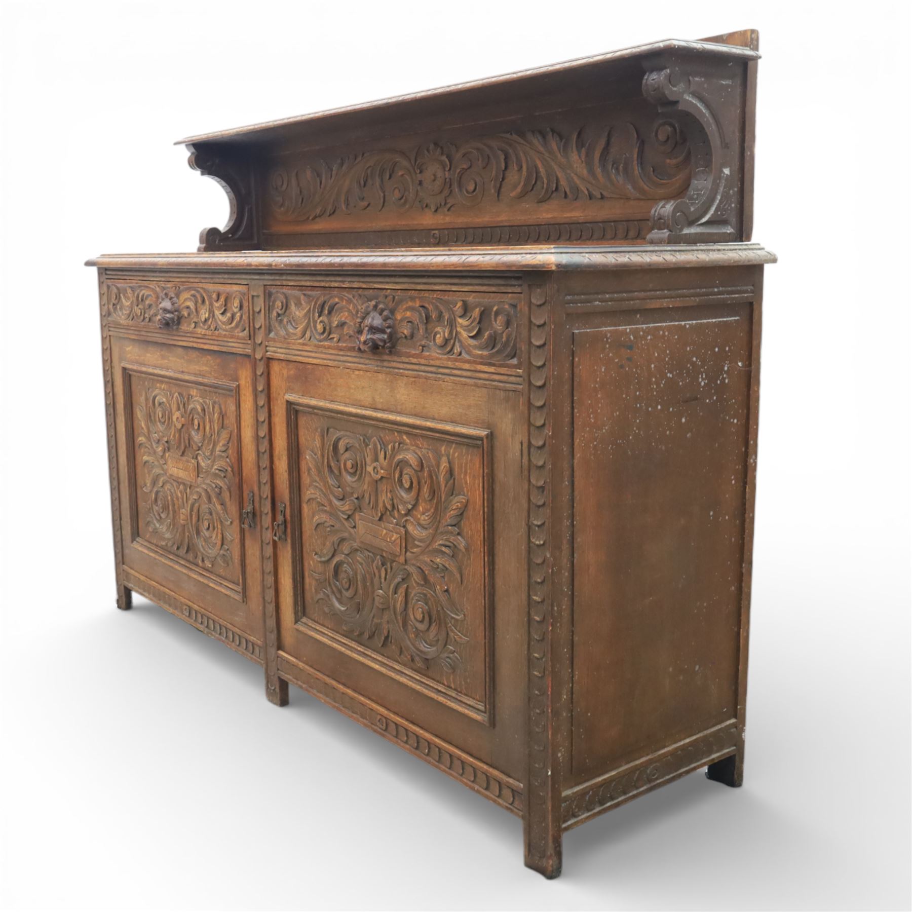 Victorian carved oak sideboard, the rectangular top with raised back carved with foliate scrolls and scroll end supports, upon a base with rectangular top with moulded edge, pair of drawers with conforming carved decoration and mask handles, and pair of carved cupboard doors, upon short stile type feet H101.5cm W183cm D54cm 