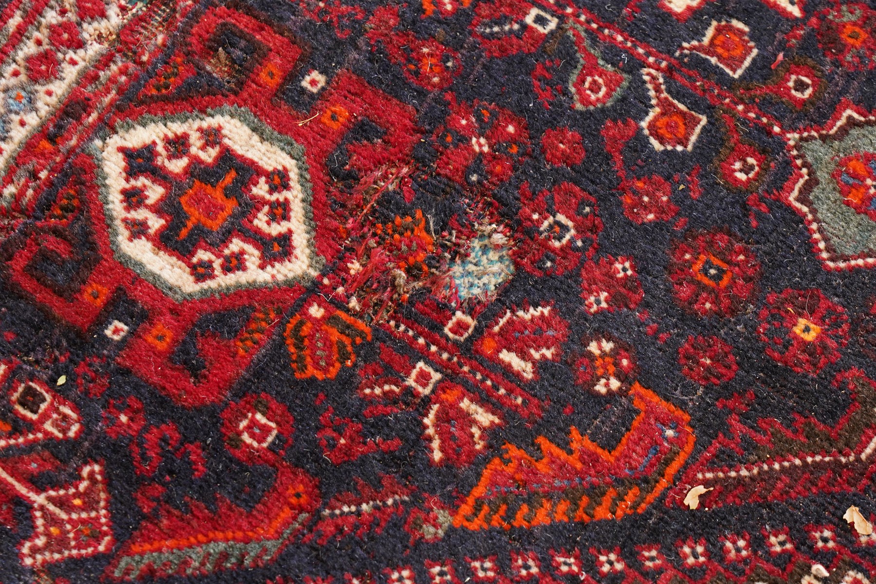 Large Persian Shiraz crimson ground carpet, the busy field decorated with a geometric pole medallion surrounded by stylised plant motifs with contrasting indigo spandrels and geometric-woven guard bands