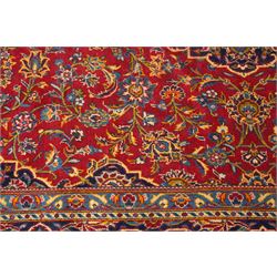 Persian Kashan hand-knotted carpet, madder red ground centred by shaped dark navy, ivory and pale blue floral medallion with pendants, surrounded by scrolling vines, palmettes and flowerheads, dark navy spandrels, enclosed by dark navy floral border with multiple floral guard stripes