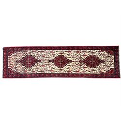 North West Persian Saveh crimson ground runner rug, the three lozenge pole medallions in an ivory field, surrounded by stylised plant motifs, the guarded border decorated with repeating geometric patterns