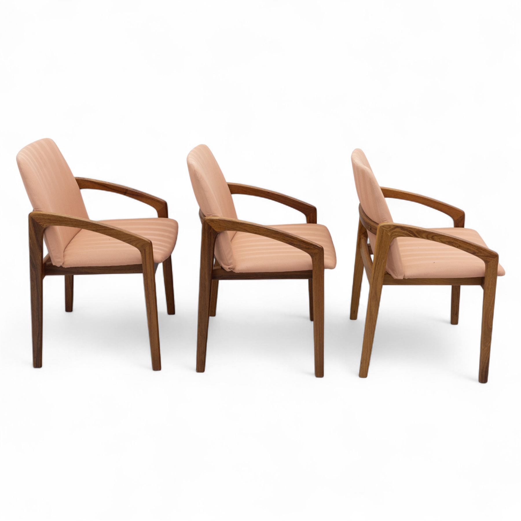 Mid-20th century Danish teak armchairs, each with curved open arms and upholstered seat and backrest in salmon pink striped fabric, raised on tapering legs