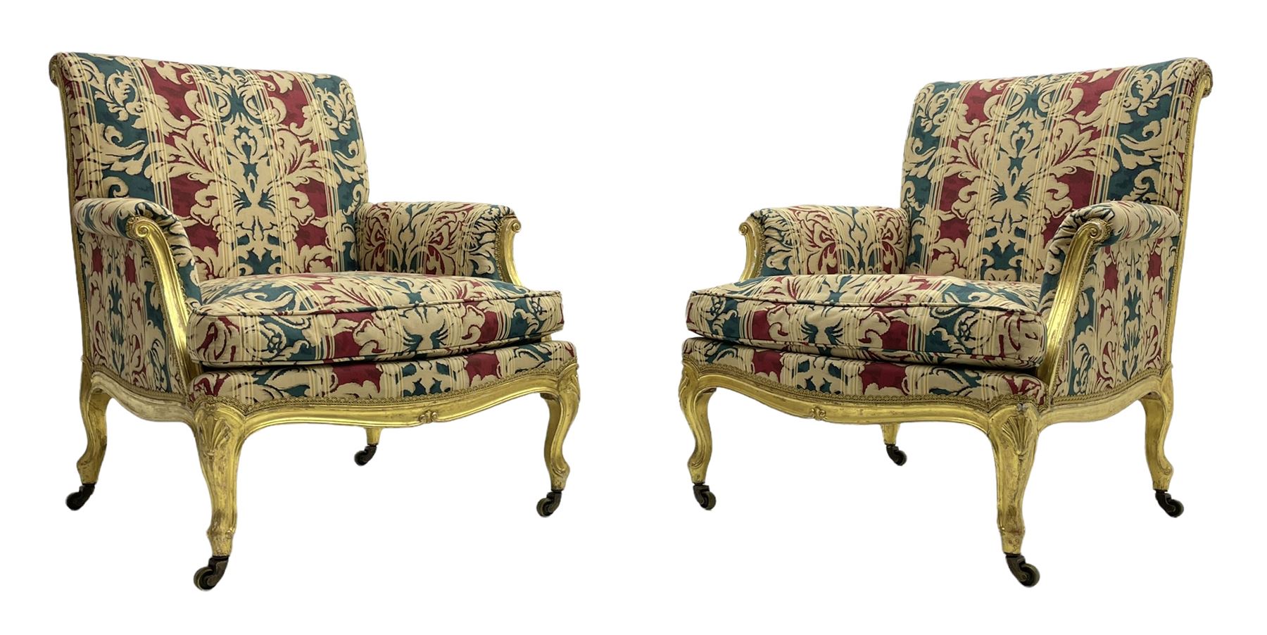 William Bertram & Son of London - pair late 19th century giltwood armchairs, moulded frame with scroll carved back and arm terminals, upholstered in striped fabric with foliate pattern, on shell carved cabriole supports, the brass castors stamped 