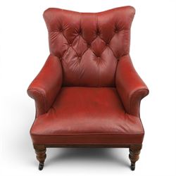 Early 20th century style oxblood red leather Chesterfield armchair, deep buttoned shaped back over padded scroll arms and loose seat cushion, raised on turned mahogany front supports with brass caps and castors