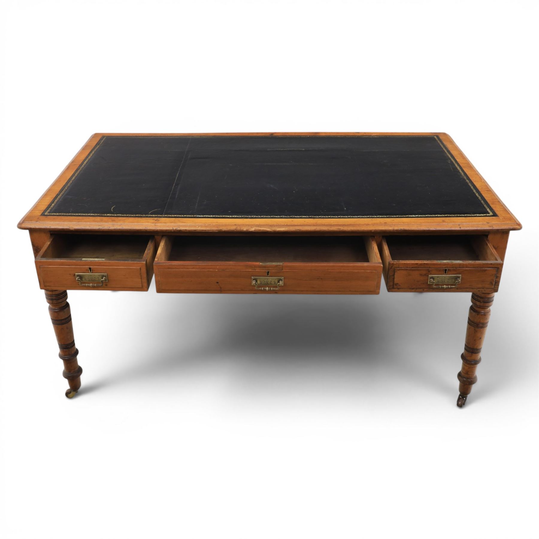 Victorian pitch pine writing table with leather inset top, rectangular top with three frieze drawers, pierced brass handles, raised on turned and fluted supports terminating in castors