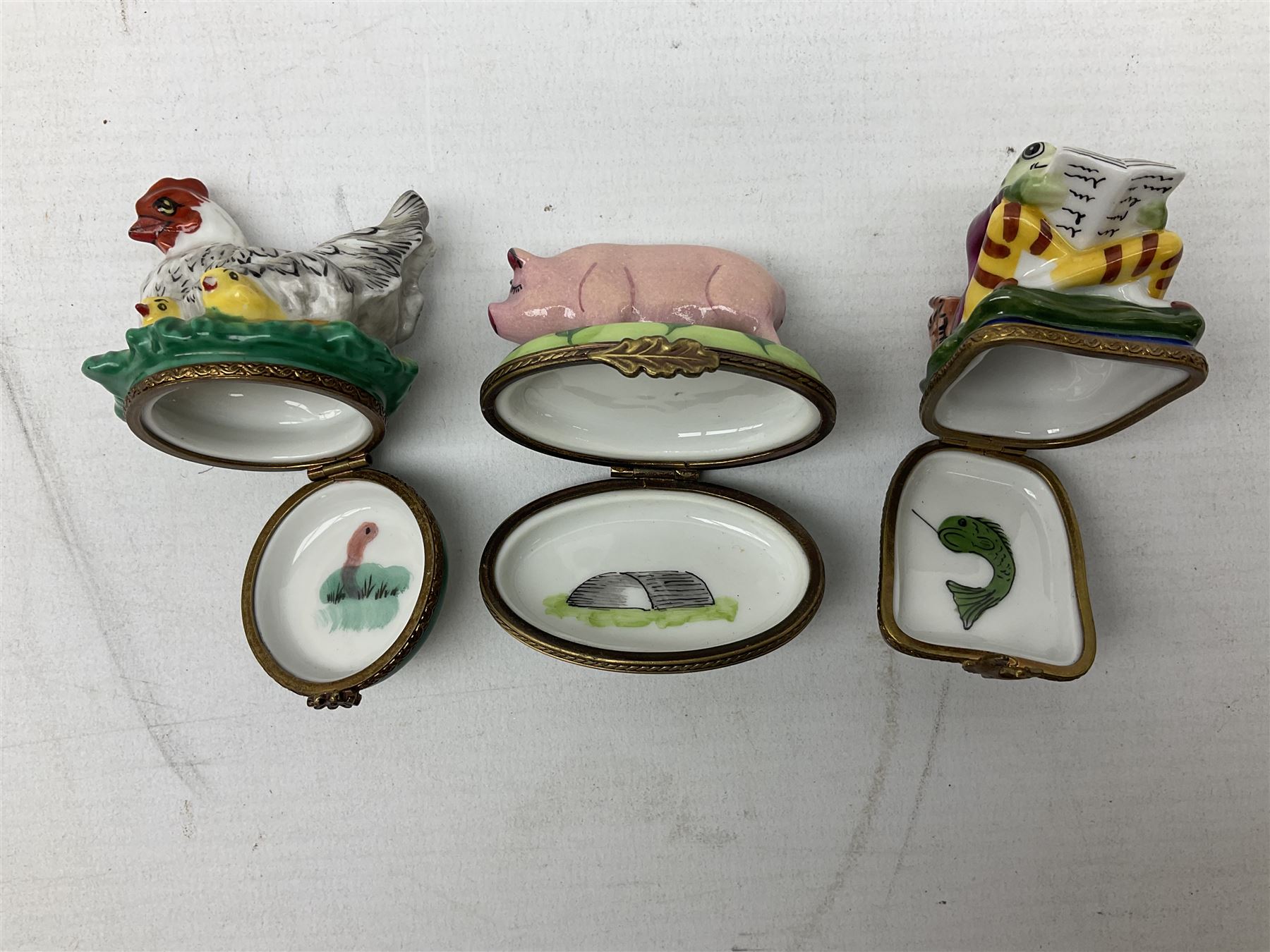 Group of Limoges trinket boxes, to include a number of novelty examples, including examples modelled as Noah's ark, shotgun case containing shotguns, picnic basket containing food, toad reading book seated upon a lily pad, etc., (9)
