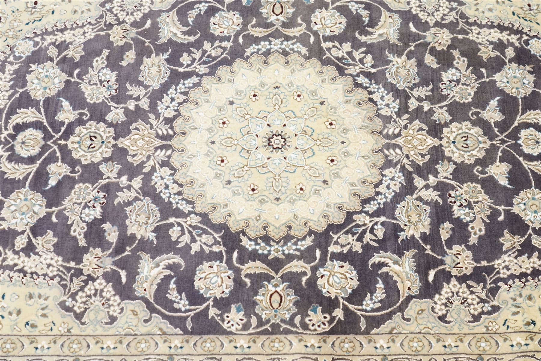 Central Persian Nain hand-knotted carpet, indigo field with central cusped medallion of radiating palmette form, enclosed with an elongated cartouche issuing network of scrolling vine work, arabesques and flowering sprays, surrounding ivory field of conforming design filled with foliate motifs and palmettes, spandrels of complimentary design with angular reserves, within principal border of ivory ground with scrolling vinery rosettes and arabesques, flanked by narrow guard stripes, with cotton fringe ends 