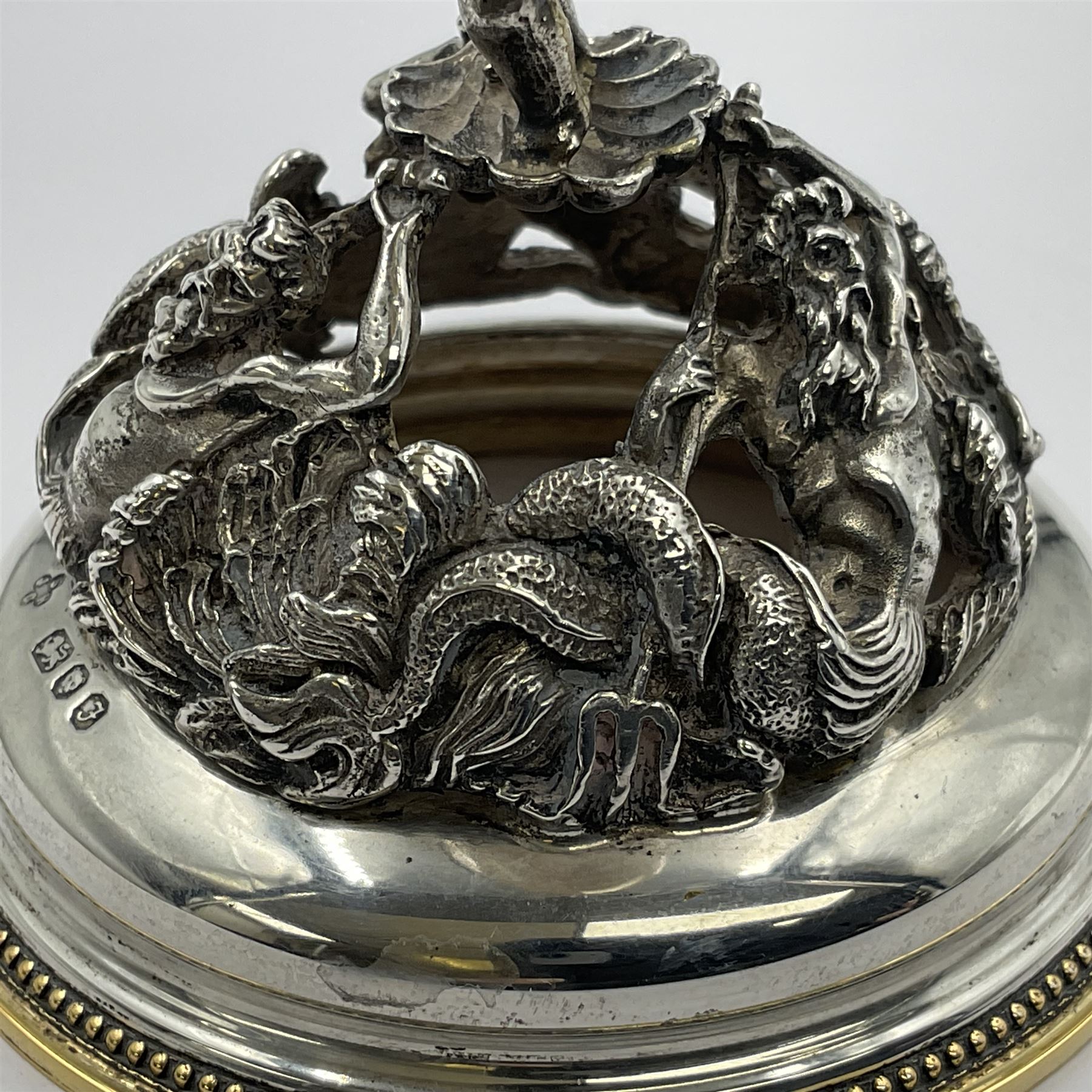 Modern limited edition silver mounted nautilus shell cup, no. 42/150, the pearlescent shell cup with silver-gilt strapwork to rim, upon a stem modelled as a putto supporting a gilt cornucopia and circular domed foot depicting Poseidon amongst swirling waves, hallmarked by St James House Company, London 1980,  H17.5cm