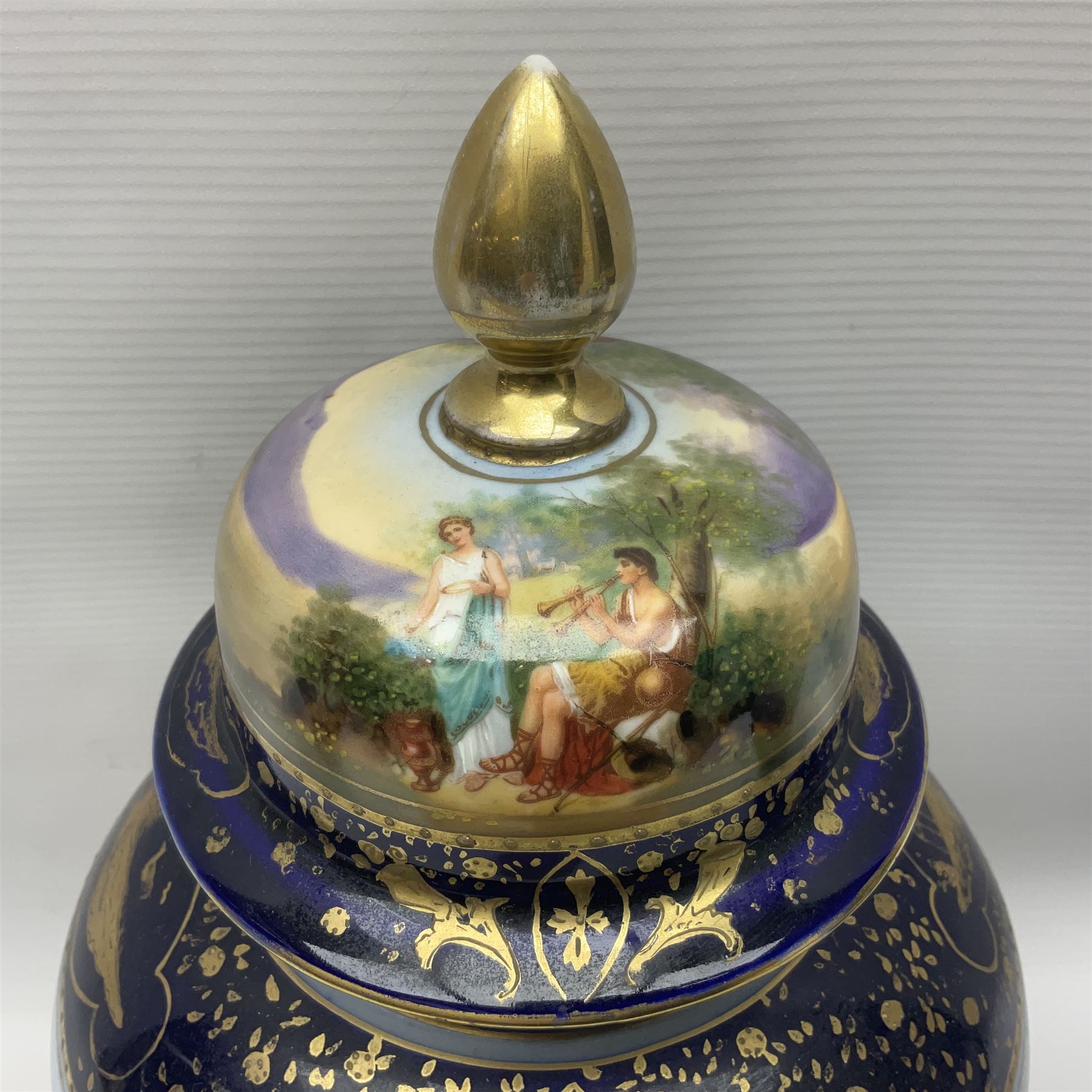 19th century Vienna style porcelain 'Musik' garniture, the central vase of baluster form with domed cover flanked by two smaller vases with twin curved gilt handles to short neck, each decorated with classical figural vignettes between blue borders heightened with gilt, H33.5cm