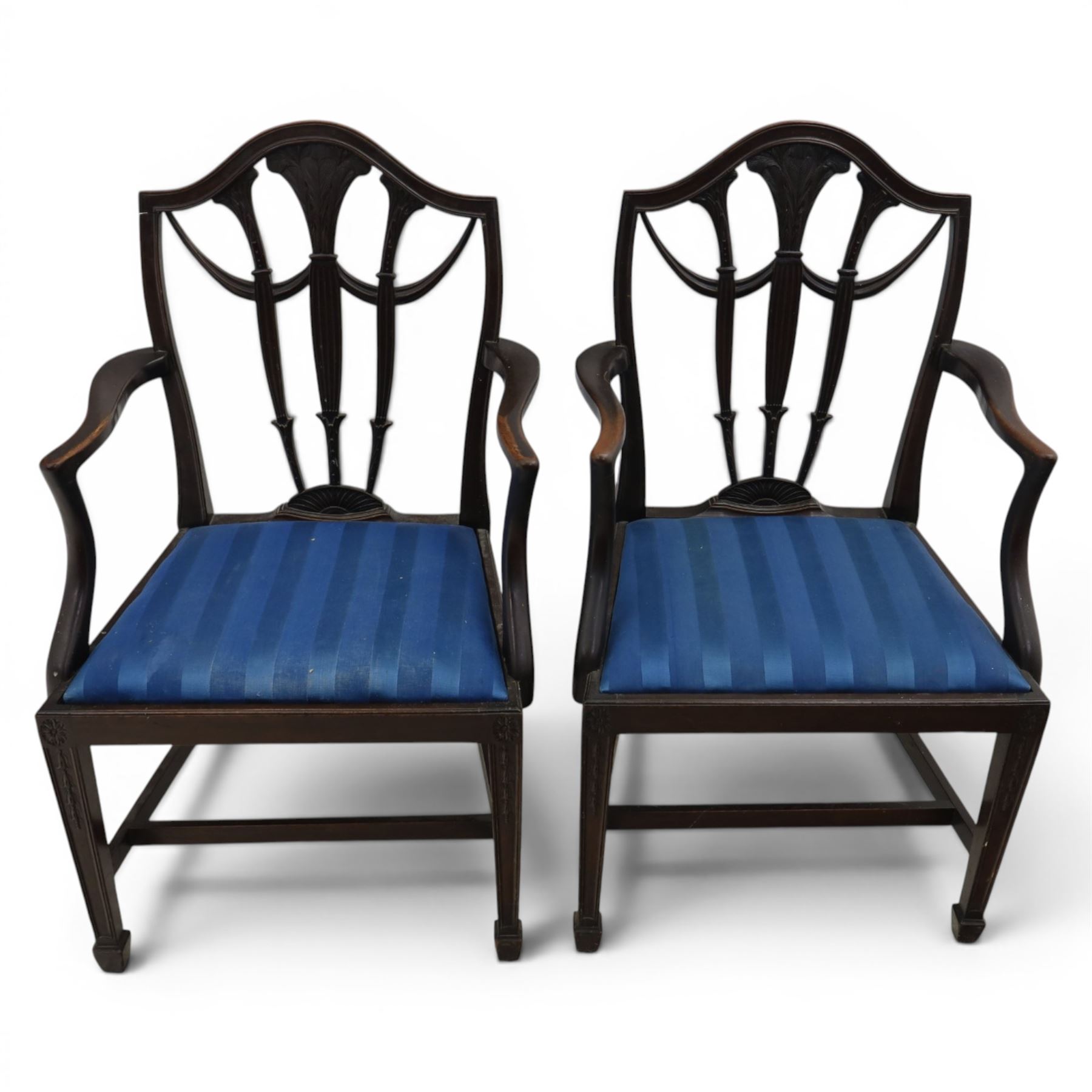 Set of eight George III style mahogany dining chairs, comprising two carvers and six singles, each with shaped top rail above pierced splay carved with feathers, with drop in stuffover seats upholstered in blue striped fabric, raised upon square tapering legs joined by stretchers, together with a mahogany twin pedestal dining table, the oval top with central leaf raised upon turned columns and splayed reeded legs terminating in lion paw feet and brass castors, 