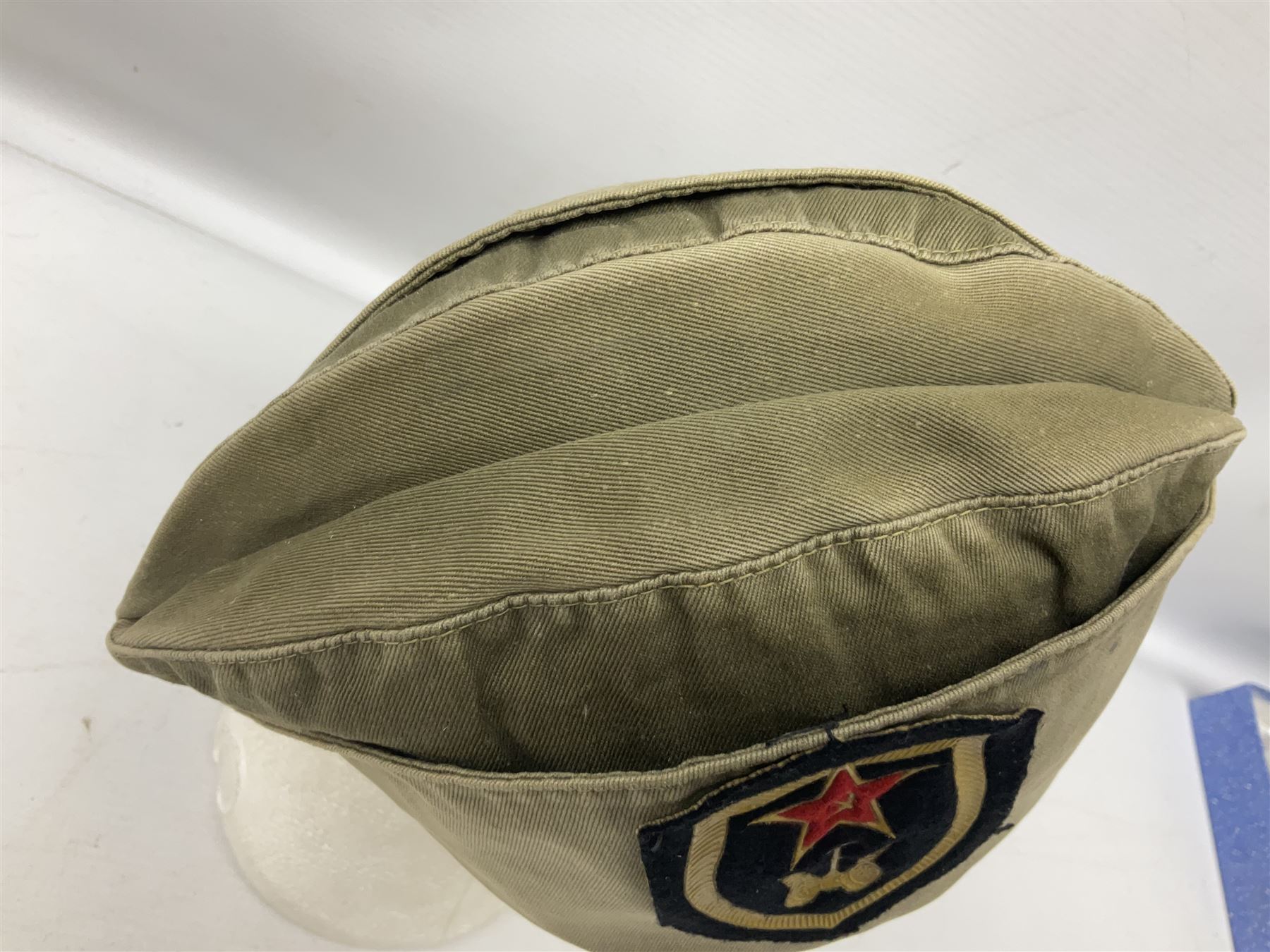 Four side caps - WW2 Russian, post-WW2 Russian and two East German; all with badges, one with multiple metal badges (4)