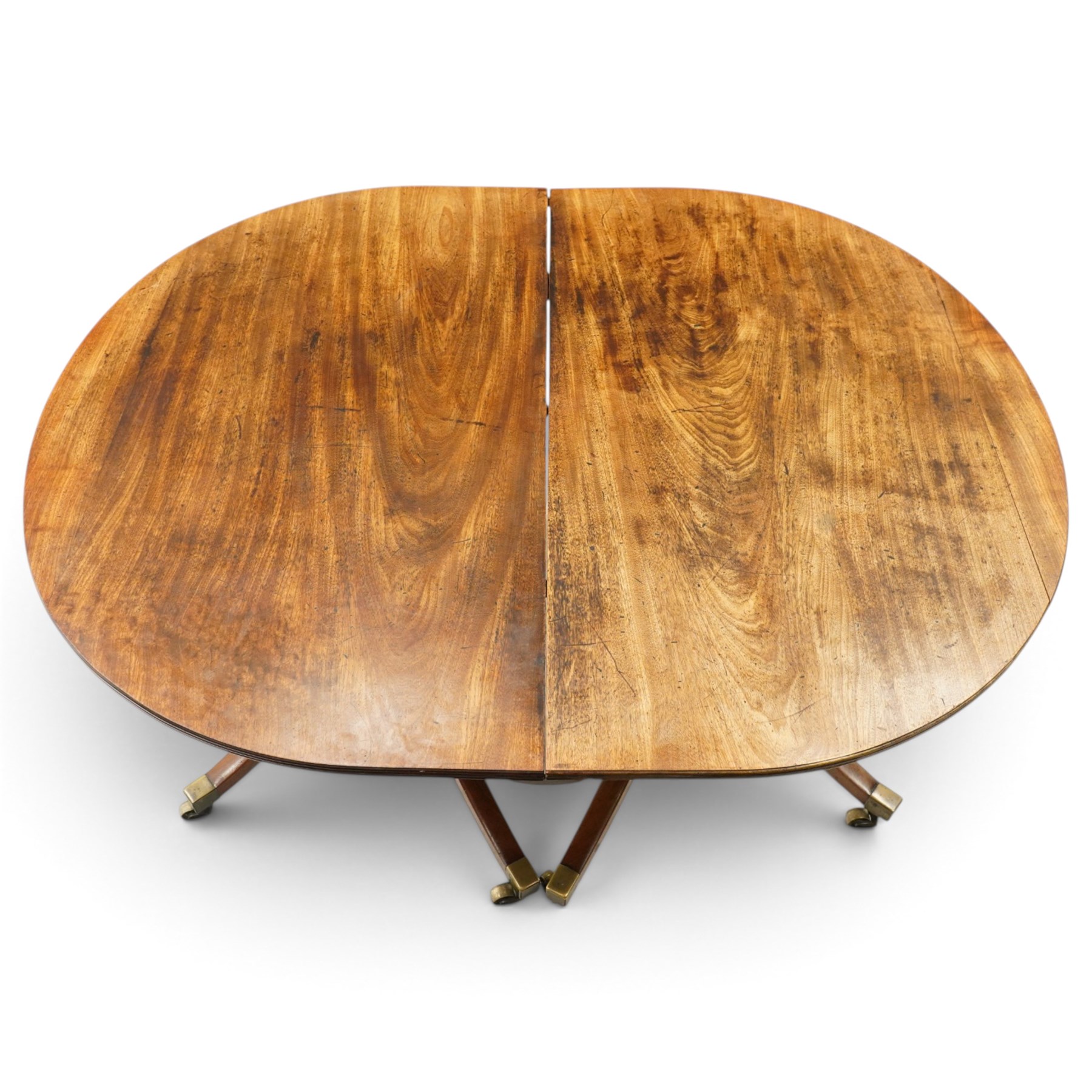 George III mahogany twin pedestal extending dining table, the twin D-ends with additional leaf, raised on twin turned pedestals terminating to four splayed supports with brass cups and castors