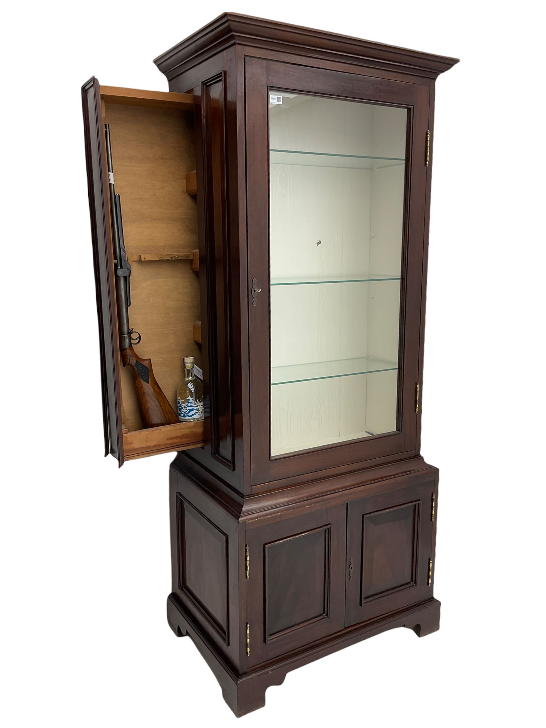 Mahogany display cabinet with hidden compartment, projecting cornice over single glazed door enclosing glass shelves, double panelled cupboard below, the interior with button releasing sliding back compartment, on bracket feet