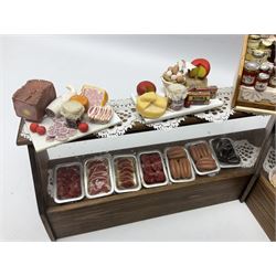 Collection of miniature dolls house grocery shop furniture and produce, comprising glazed corner counter with brass style cash register, shelved preserves unit, pies, cheese board and trays of meats, pair of white cheese counters, biscuit display with six tins, glazed preserves cabinet, pair of shop chairs and four further cheese boards complete with grapes and label flags
