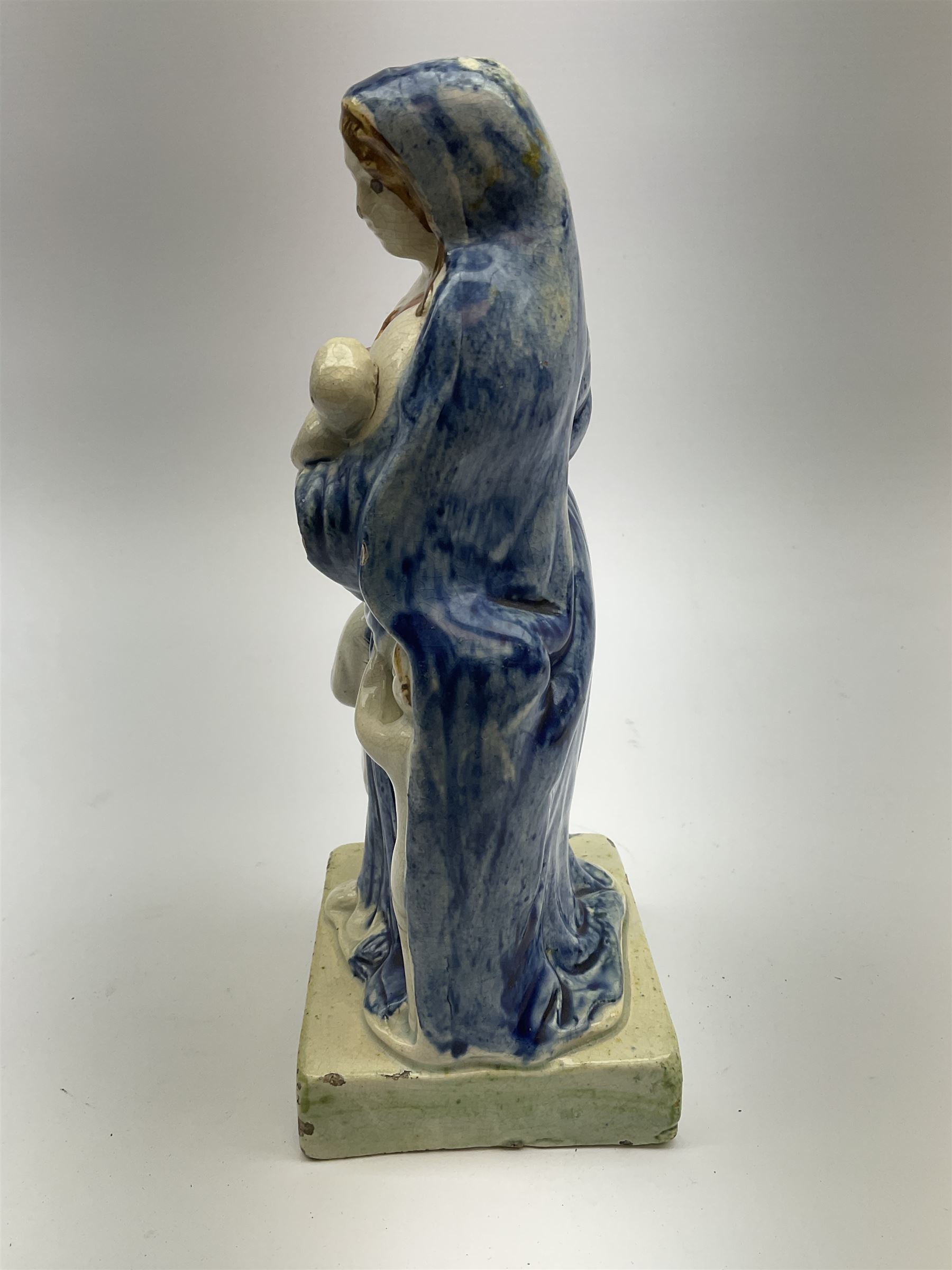 Late 18th century Prattware figure representing Charity, modelled as a mother with baby in her arms and two small children clutching at her robes, upon a square base, overall H21cm.