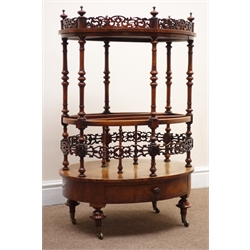  Victorian figured walnut oval Canterbury, pierced galleried top with turned finials, three division base with pierced band and single drawer on mushroom turned supports with brass sockets and castors, W63cm, D45cm, H93cm  