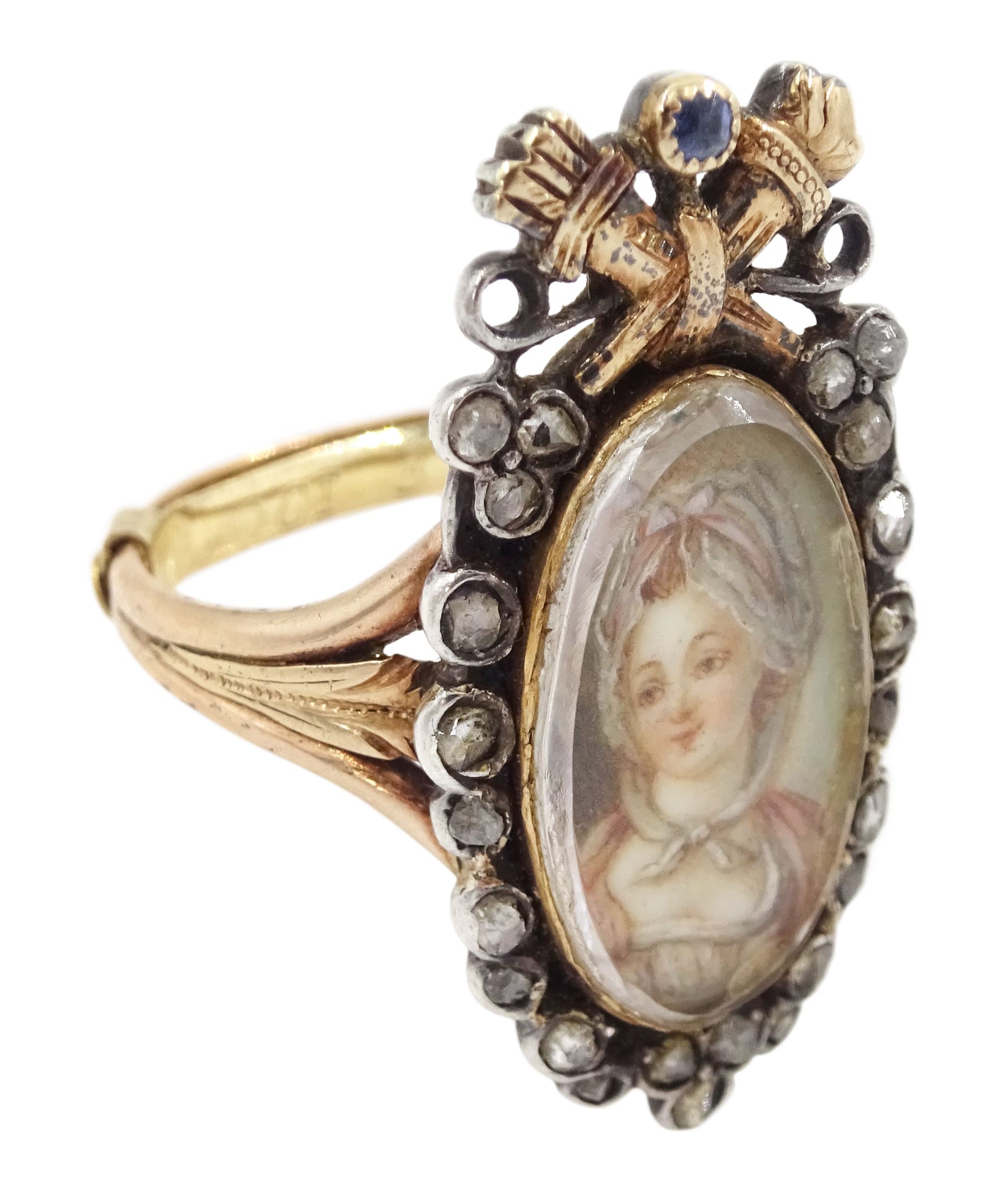18th / 19th century silver and gold diamond and sapphire portrait ring, set with an oval miniature of a woman wearing a bonnet on ivory, under a glazed panel, surmounted with a 'trophy of love' symbol, modelled as a flaming torch and bow and quiver, set with a single round cut sapphire and rose cut diamond surround, to trifurcated shoulders, on French 18ct gold shank, Eagle hallmark. This lot has been registered for sale under Section 10 of the APHA Ivory Act