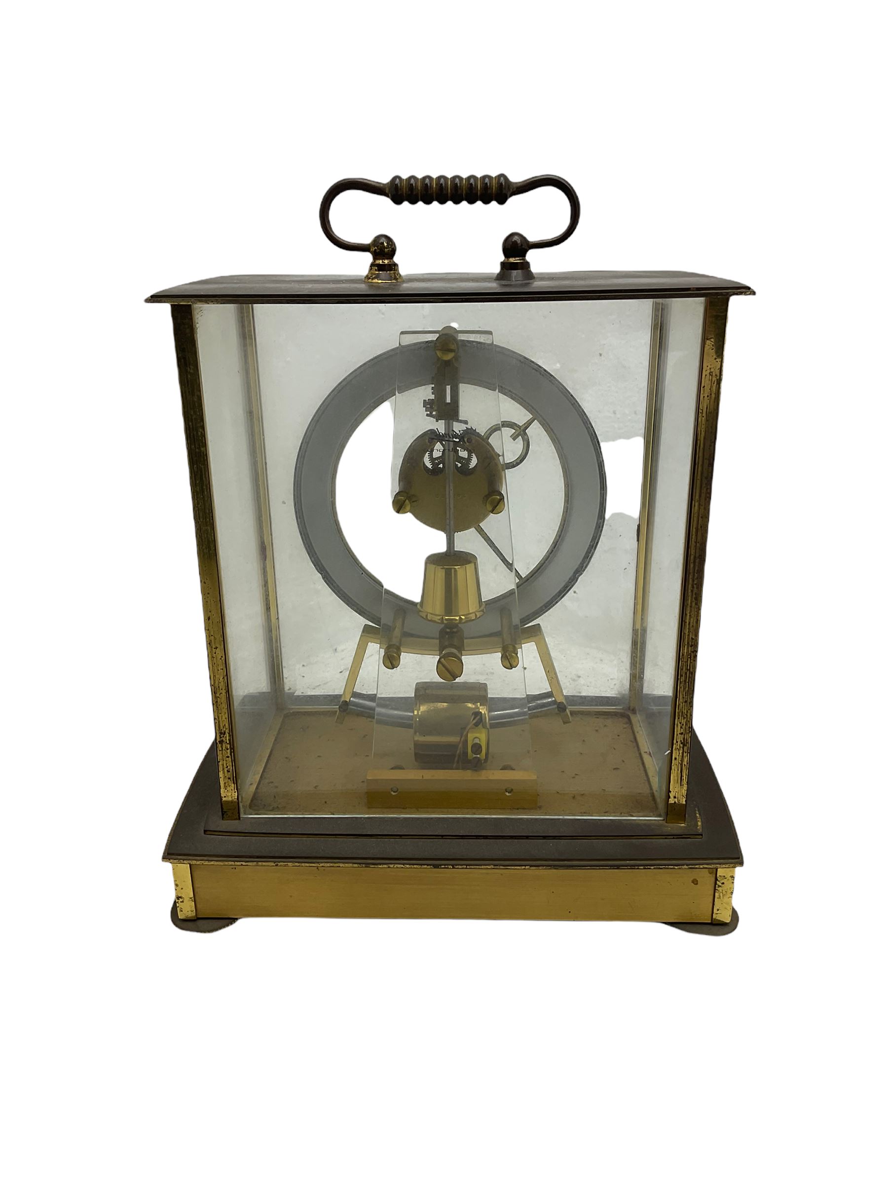 A  mid-20th century German Kieninger & Obergfell, “Kundo” battery operated 
mantle clock, rectangular case with four bevelled viewing panels and carrying handle, electrically operated solenoid pendulum powered via a battery housed in the base, skeleton movement with a visible escapement viewed through an open chapter ring with Arabic numerals and gilt baton hands.

