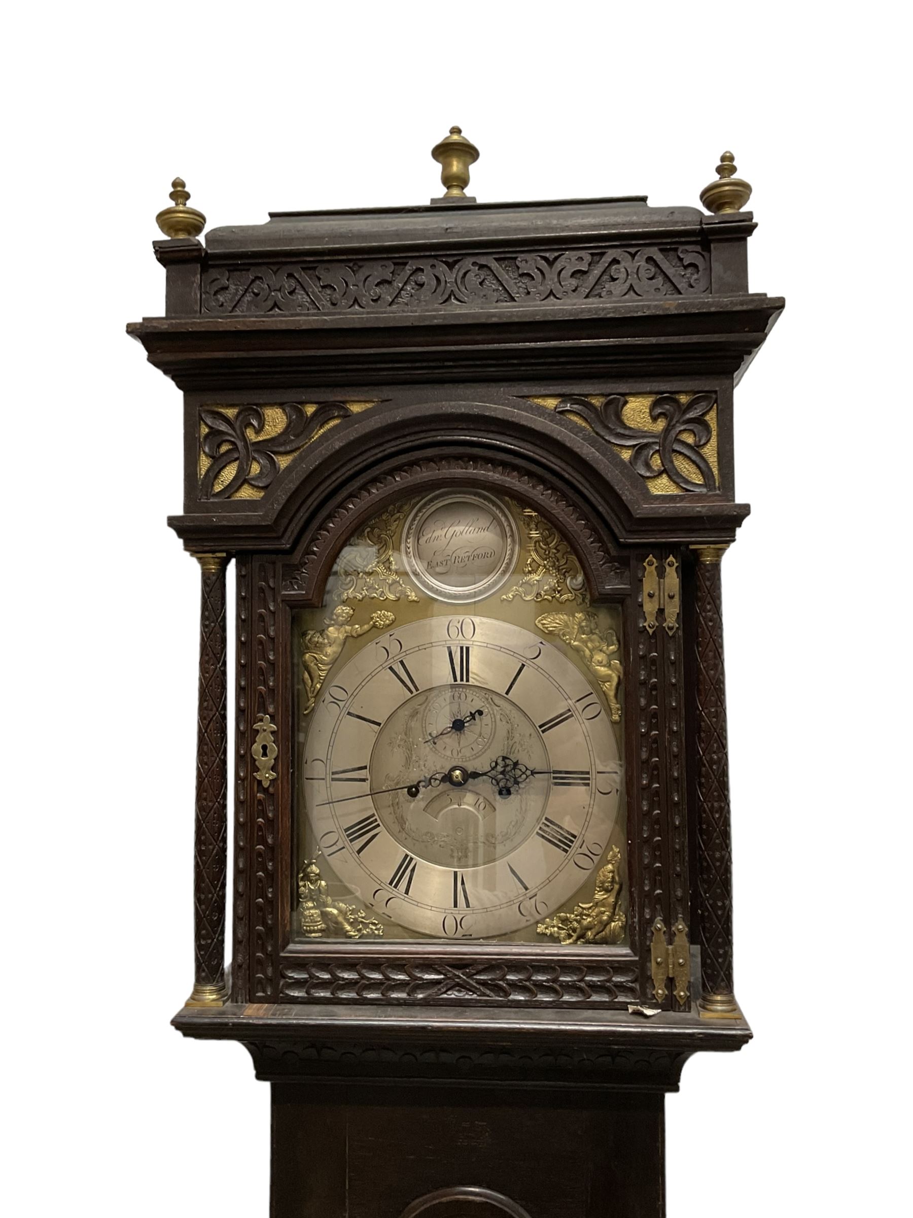 Edward Golland of Retford (Notts) - mid-18th century 8-day carved oak longcase c1760 , with a stepped caddy top and blind fret, break arch hood door flanked by carved pilasters with brass capitals,  trunk with a carved break arch toped door on a carved plinth with applied skirting and feet, brass dial with matching steel hands, silvered and engraved dial centre and chapter ring, with seconds dial and calendar aperture, four seasons spandrels and boss to the arch with makers name, four pillar rack striking movement, striking the hours on a bell. With weights and pendulum.            
Edward Golland is recorded as working in Retford during the late 18th century.