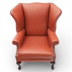 Georgian design red leather wingback armchair, with shaped back and scrolled arms, and close brass studded trim, upon cabriole front legs with claw and ball feet