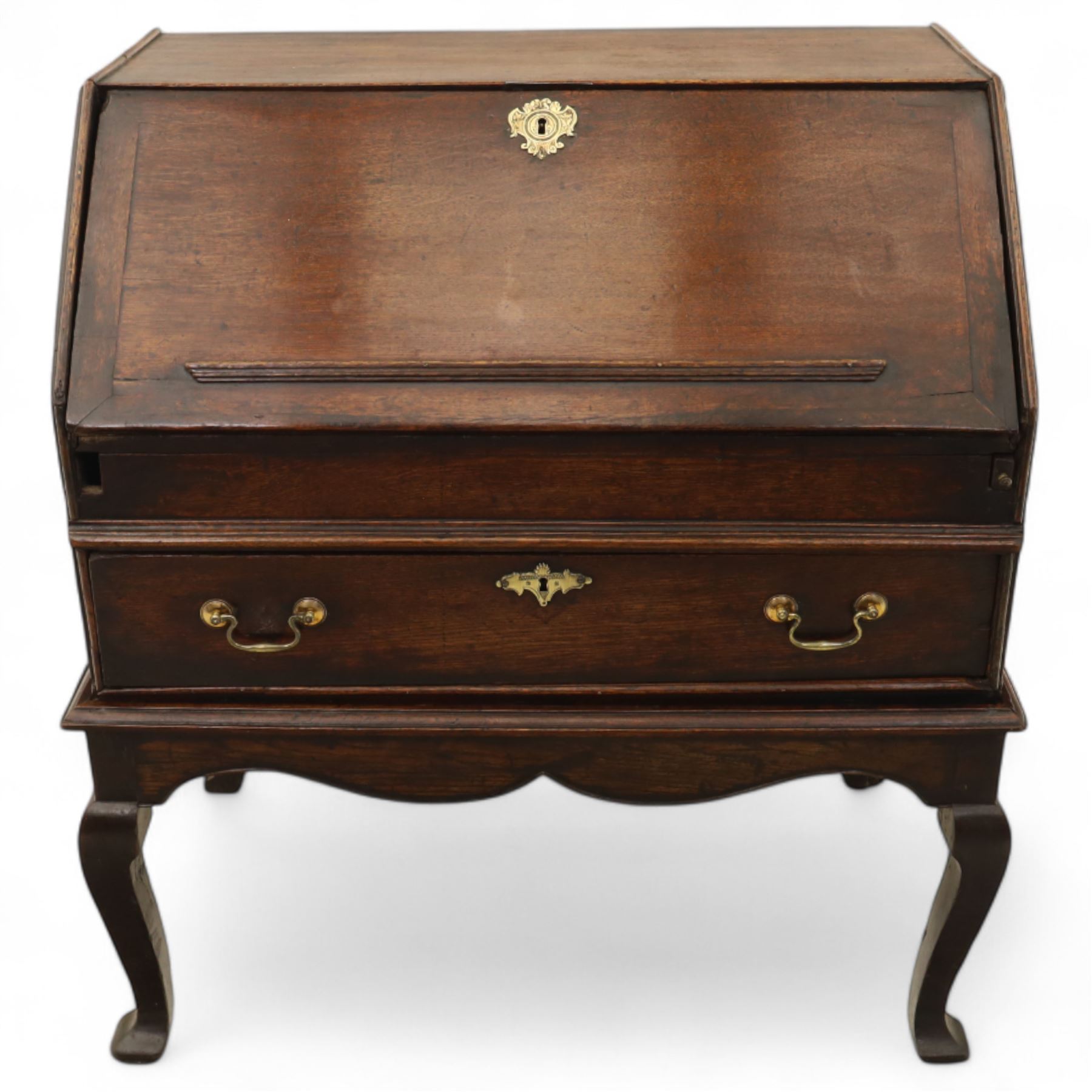 Early 18th century George I oak bureau on original stand, the fall front enclosing an arrangement of correspondence drawers and pigeonholes over central well, fitted with single long drawer below, the shaped apron over cabriole supports with pad feet