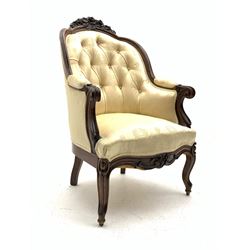 Victorian rosewood armchair, the shaped cresting rail carved with flowers and foliage, moulded frame, upholstered in buttoned cream patterned fabric, scrolled arm terminals and supports, shaped apron carved with flower heads, cabriole supports with castors