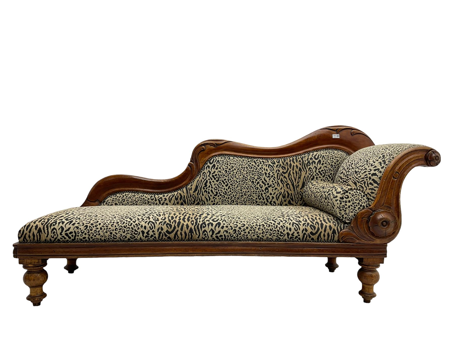 Victorian mahogany framed chaise longue, shaped arm carved with acanthus leaves, the scrolled back with applied carved rosettes,upholstered in monochrome leopard print fabric with bolster cushion, raised on turned supports