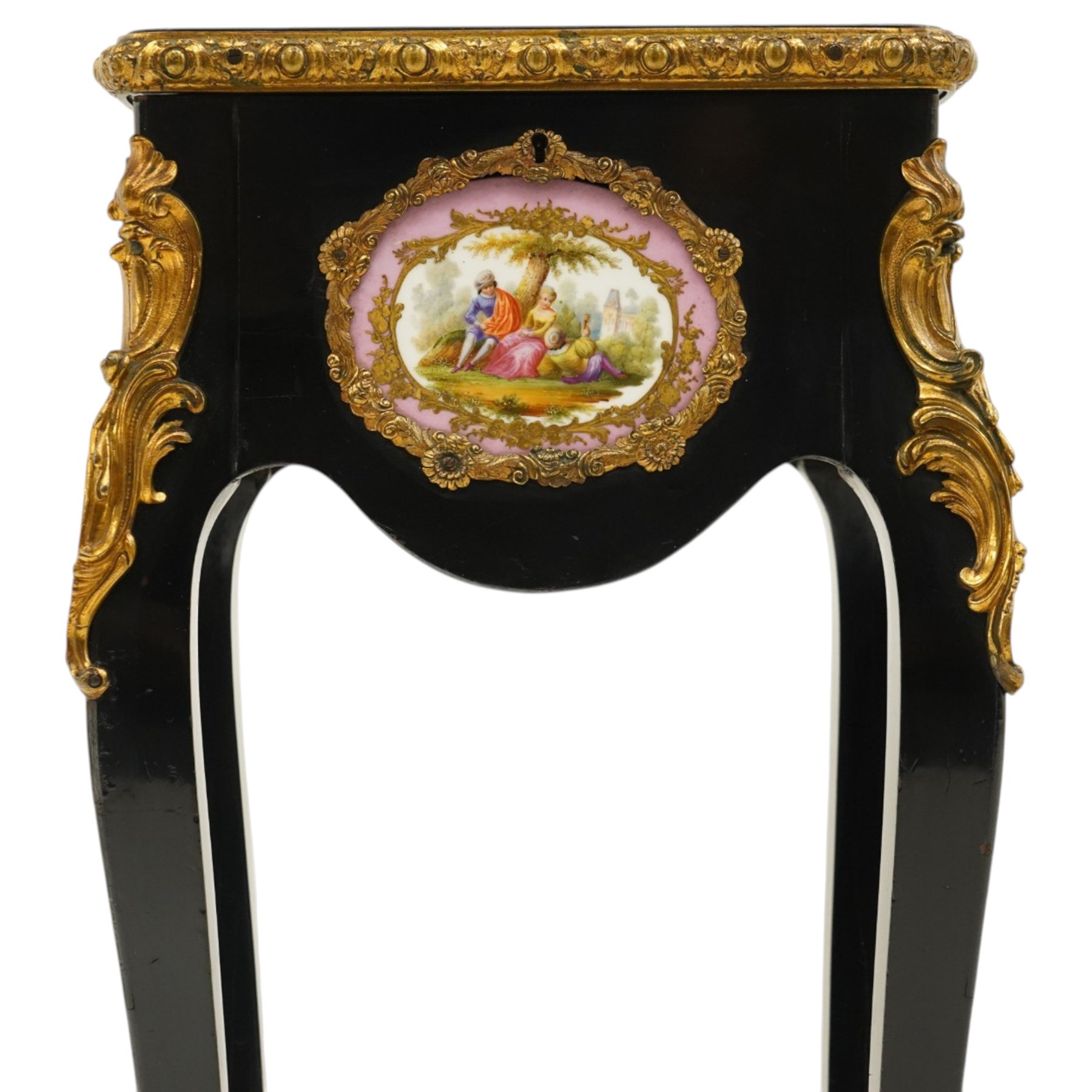 Early 20th century French ebonised sewing or work table, rectangular hinged top with foliate moulded gilt metal edge, enclosing upholstered interior, over a central Sevres style porcelain plaque depicting a courting scene, raised on cabriole supports with gilt metal carotuche and acanthus knee mounts, united by undertier with brass gallery terminating to gilt metal scroll feet