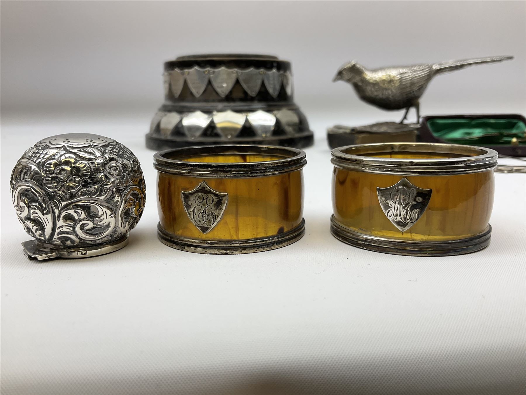 Group of silver, to include filled figure of a pheasant, hallmarked for London, pair of silver mounted horn napkin rings, miniature Edwardian bible with silver cover embossed with putti, Victorian silver brooch, ebonised plinth with applied inscribed silver shields, etc., together with two stick pins, one example with 9ct gold terminal 