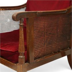 Pair of early 20th-century mahogany Bergère armchairs in the manner of Gillows, the back and seat with woven cane panels with loose red velvet cushions, the frame with swept arms with tapered and reeded uprights, raised on tapered square-section front legs terminating in brass cup castors 