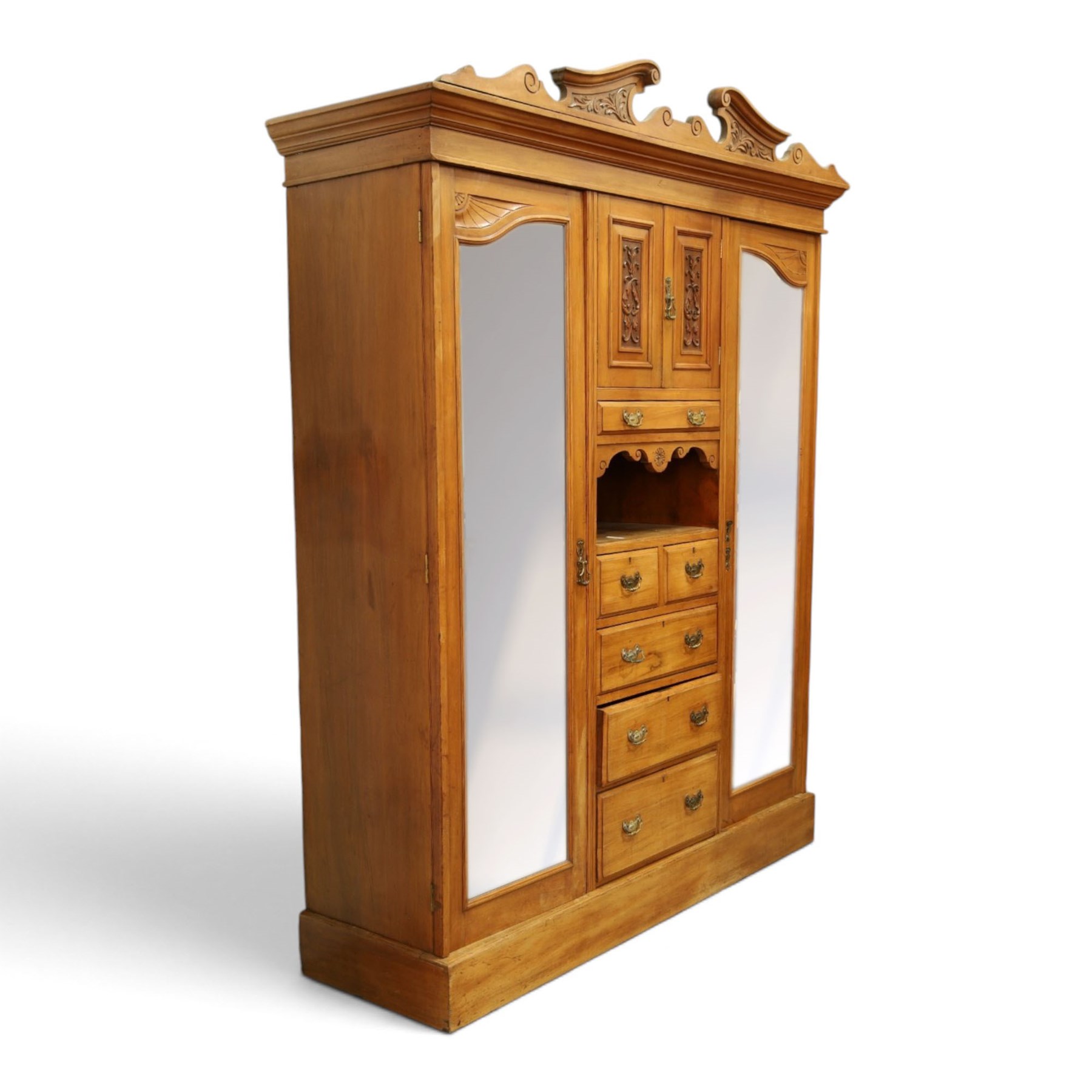 Edwardian walnut triple combination wardrobe, projecting pediment with pierced foliate scroll cresting above a central cupboard flanked by bevelled mirrored doors, over open recess with mirrored back, above two short and three long drawers with brass handles, interior fitted with hanging rails and shelf, raised on plinth base
