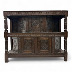 Early 20th-century  oak Jacobean two-tier revival court cupboard, rectangular top with carved notch and stylized foliate carved edge above a carved lozenge pattern frieze and a central cupboard with carved geometric designs and geometric carved panelled sides, above a carved panelled cupboard with two doors of similar geometric design, the whole flanked by two sets of stop-fluted baluster turned columns and supported on stile feet