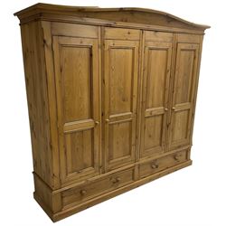 Large pine quadruple wardrobe, the arched pediment over four panelled doors, the base fitted with two long drawers