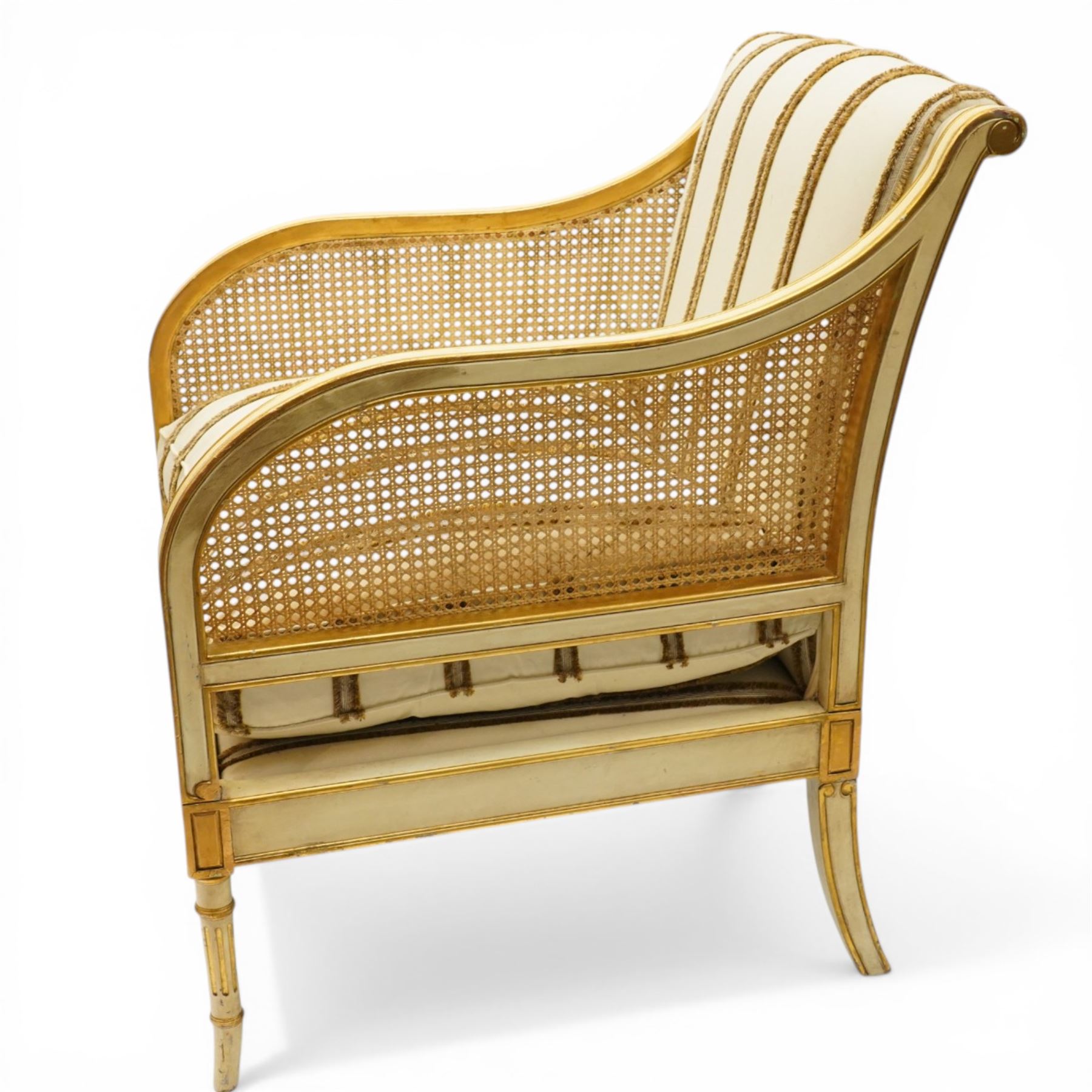 Louis XV design cream painted and parcel-gilt bergere armchair of large proportions, high scrolled back over canework arms, upholstered in striped fabric with over-stuffed loose seat cushion, on fluted supports