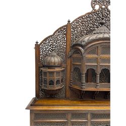 Late 19th century Indian Burmese carved and pierced hardwood and brass inlaid wall shelf, the shaped back profusely decorated with trailing and interlaced foliage, with projecting architectural structures, the central balcony with canopy top and five open windows with arched apertures on columns, two flanking five-sided balconies, the shelf supported by six foliate carved columns with pierced cusped pointed arches 